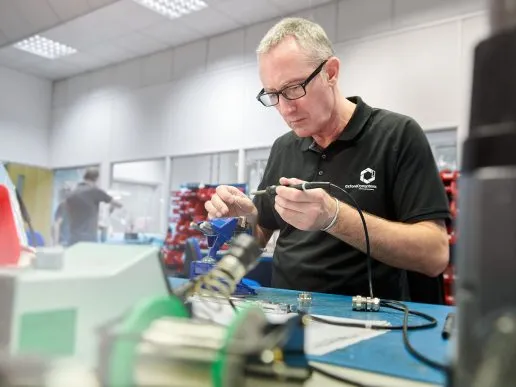 An engineer solders components for a Cryostream system, showcasing precision and focus.